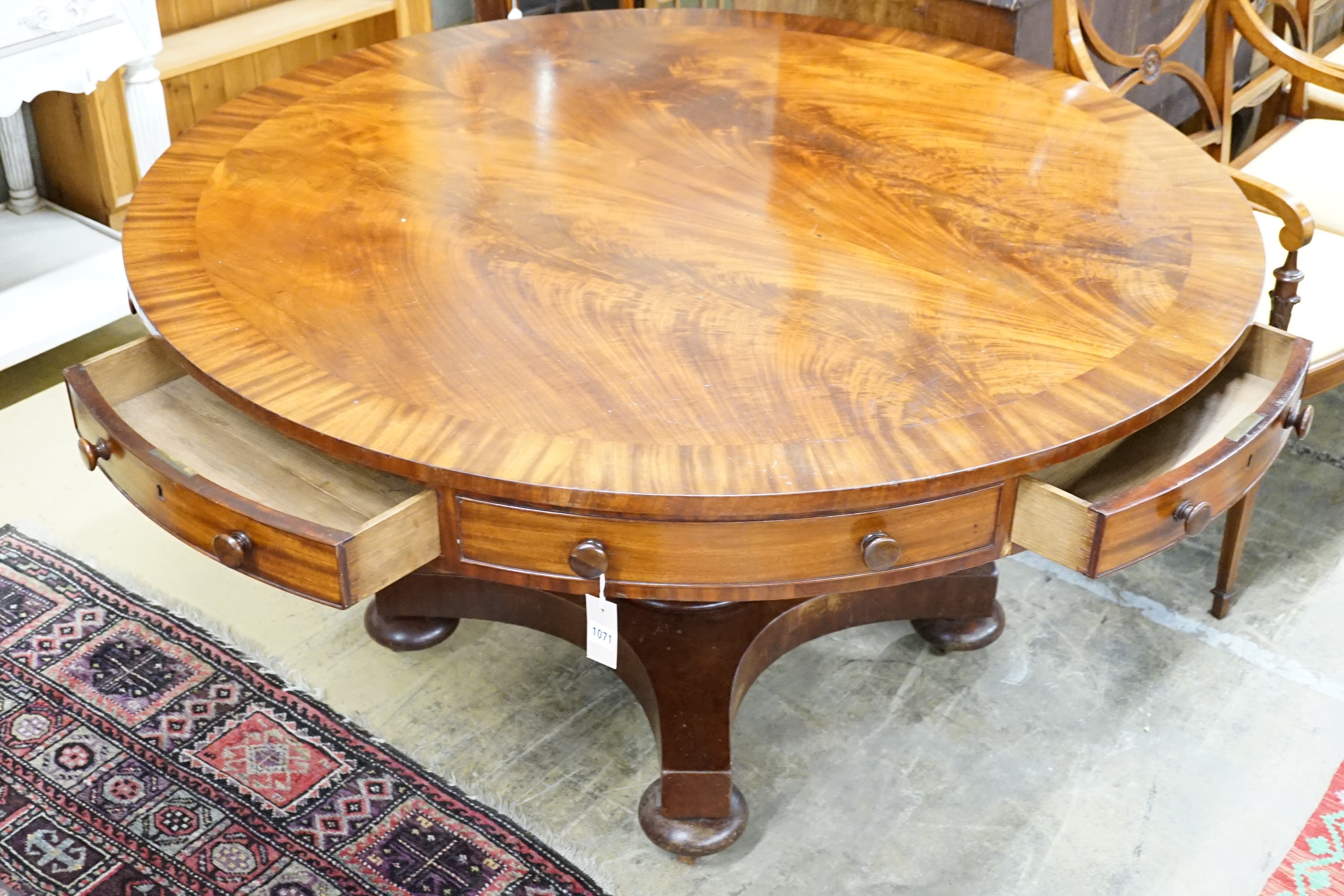An early Victorian flame mahogany drum top ‘rent’ table, fitted four drawers on turned column saltire platform and brass castors, diameter 138cm, height 74cm